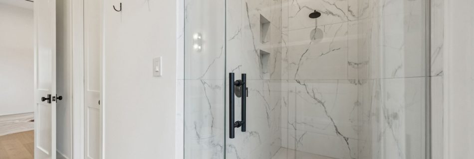 Glass walk-in shower with marble-look tile in a Bellaire new construction home