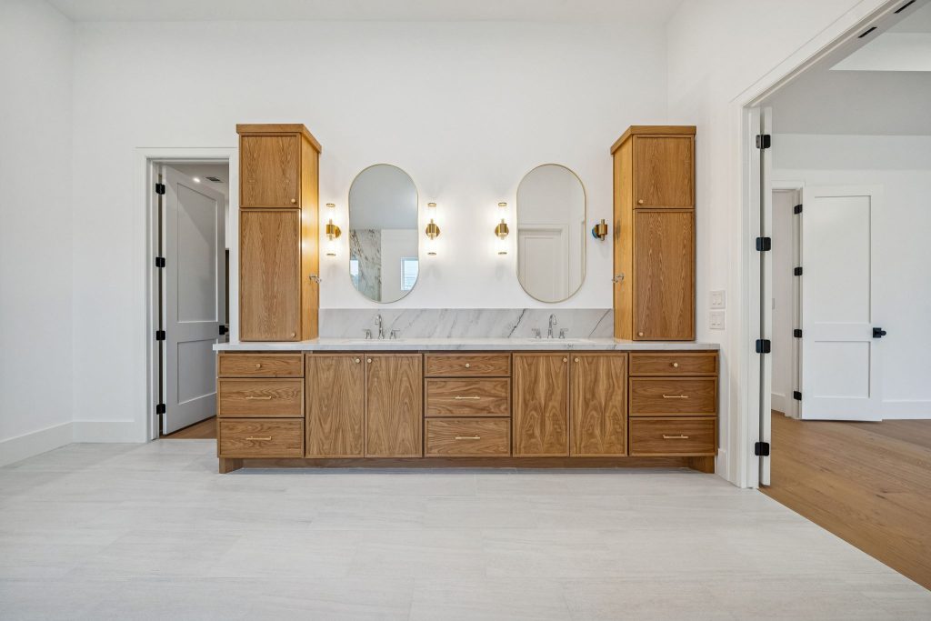 Double vanity with wood cabinets and oval mirrors in a Bellaire custom home primary bath